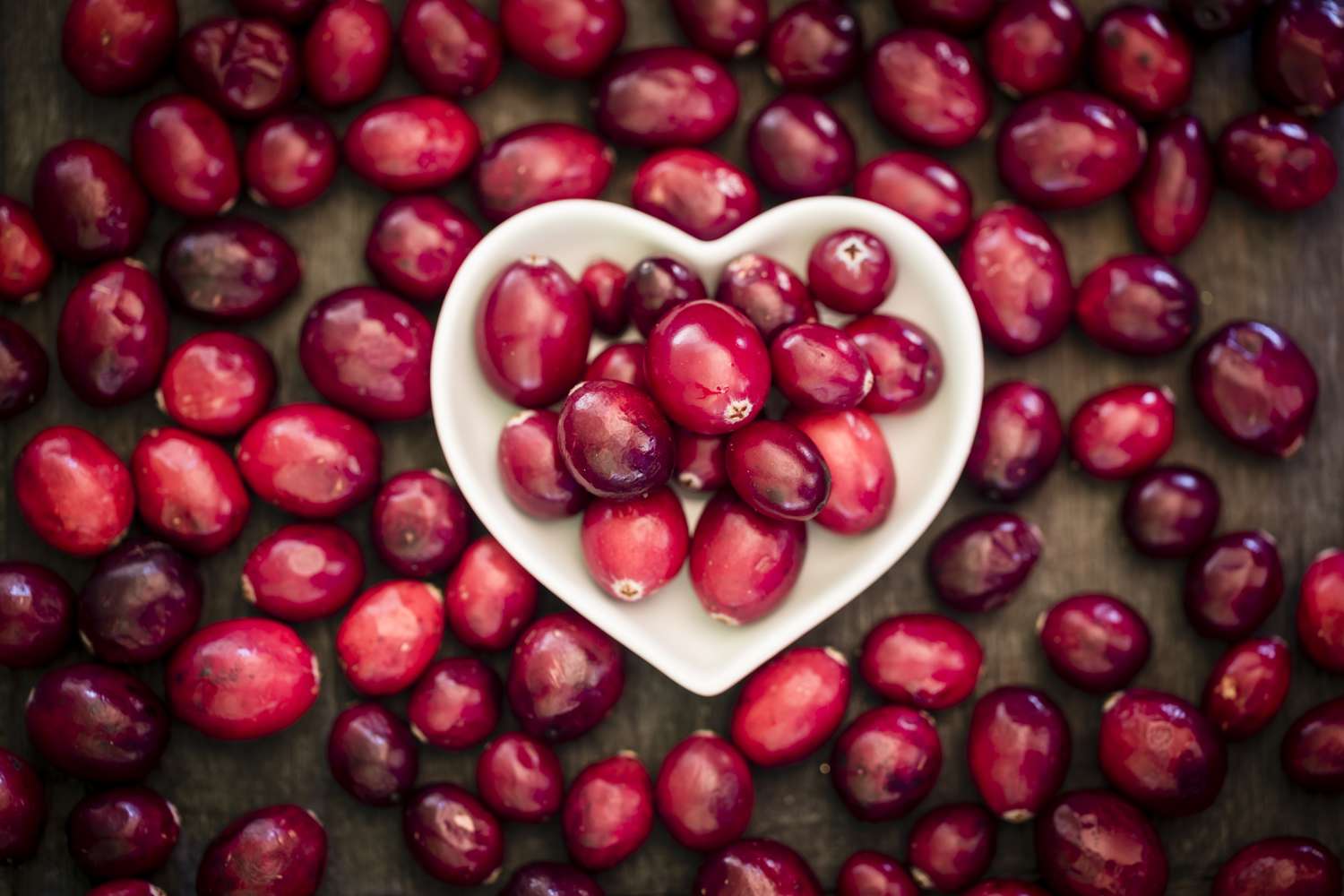 Bowl of cranberries surrounded by cranberries on wooden table, elevated view